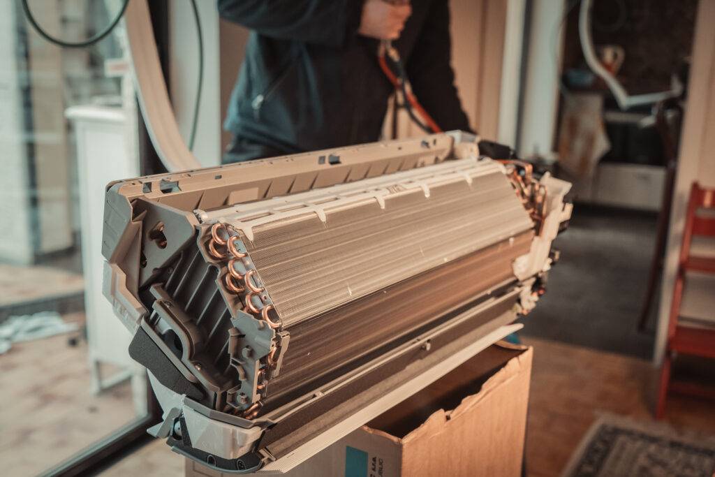 Installateur draagt de binnenunit van een airco met de warmtewisselaar en de ventilatorrol in het zicht